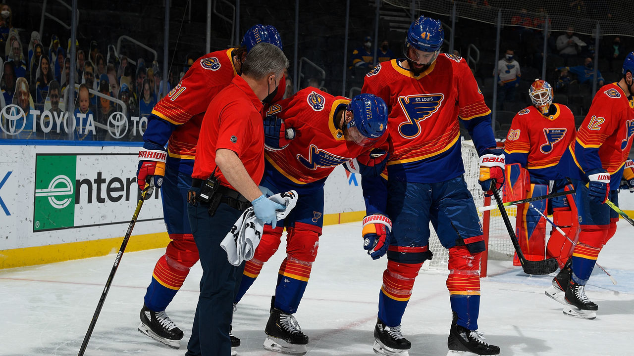 ST. LOUIS, MO - FEBRUARY 22: Carl Gunnarsson is helped off of the ice by trainer Ray Barile and Robert Bortuzzo #41 of the St. Louis Blues on February 22, 2021 at the Enterprise Center in St. Louis, Missouri.