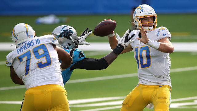 INGLEWOOD, CALIFORNIA - SEPTEMBER 27: Justin Herbert #10 of the Los Angeles Chargers passes the ball under pressure from Brian Burns #53 of the Carolina Panthers during the second half of a game against the Carolina Panthers at SoFi Stadium on September 27, 2020 in Inglewood, California.