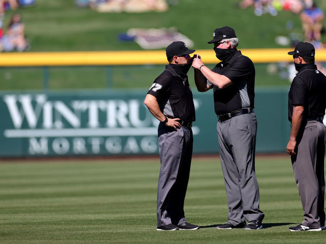 MESA, ARIZONA - MARCH 02: Umpire Jim Reynolds #77 gets some help with his mask during the third inning of a preseason game between the Kansas City Royals and the Chicago Cubs on March 02, 2021 in Mesa, Arizona.