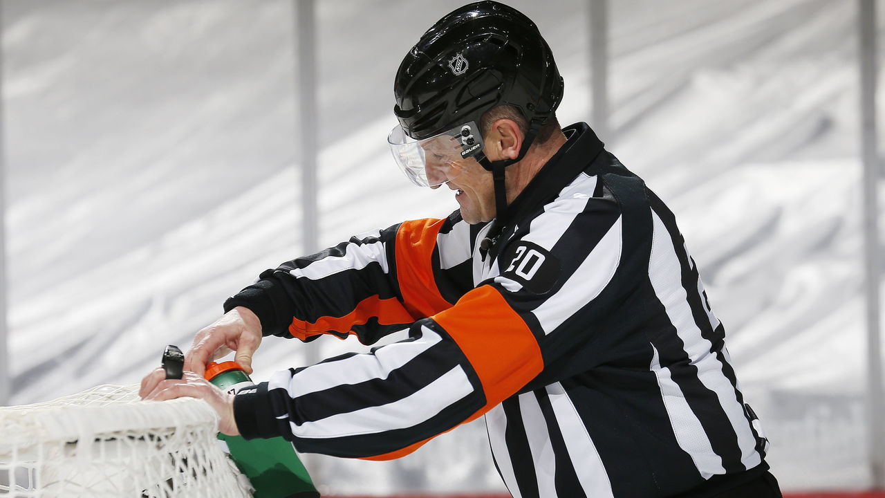 NEWARK, NJ - MARCH 2: Refee Tim Peel #20 fixes the water bottle on the net during the game between the New York Islanders and the New Jersey Devils at Prudential Center on March 2, 2021 in Newark, New Jersey.