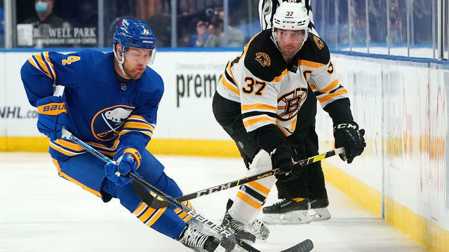 BUFFALO, NY - MARCH 18: Patrice Bergeron #37 of the Boston Bruins flips the puck past Taylor Hall #4 of the Buffalo Sabres during the third period at KeyBank Center on March 18, 2021 in Buffalo, New York.
