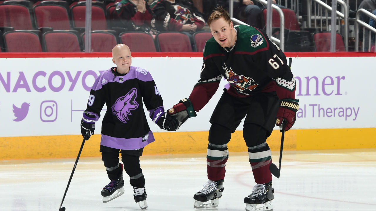 GLENDALE, ARIZONA - NOVEMBER 16: Eight-year old Leighton Accardo, who is battling germ cell cancer, skates with Lawson Crouse #67 of the Arizona Coyotes prior to an NHL game between the Arizona Coyotes and Calgary Flames at Gila River Arena on November 16, 2019 in Glendale, Arizona. Accardo signed an honorary one day player contract with the Coyotes as part of the Hockey Fights Cancer initiative.