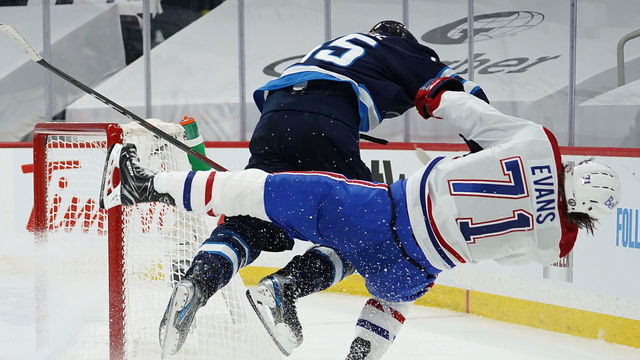 WINNIPEG, MB - JUNE 2: Jake Evans #71 of the Montreal Canadiens is checked hard by Mark Scheifele #55 of the Winnipeg Jets after Evans's third-period empty-net goal in Game One of the Second Round of the 2021 Stanley Cup Playoffs on June 2, 2021 at Bell MTS Place in Winnipeg, Manitoba, Canada. Evans was injured on the play.