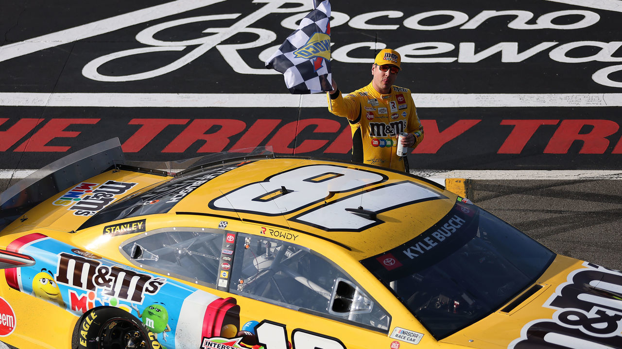 LONG POND, PENNSYLVANIA - JUNE 27: Kyle Busch, driver of the #18 M&M's Mini's Toyota, celebrates with the checkered flag after winning the NASCAR Cup Series Explore the Pocono Mountains 350 at Pocono Raceway on June 27, 2021 in Long Pond, Pennsylvania.