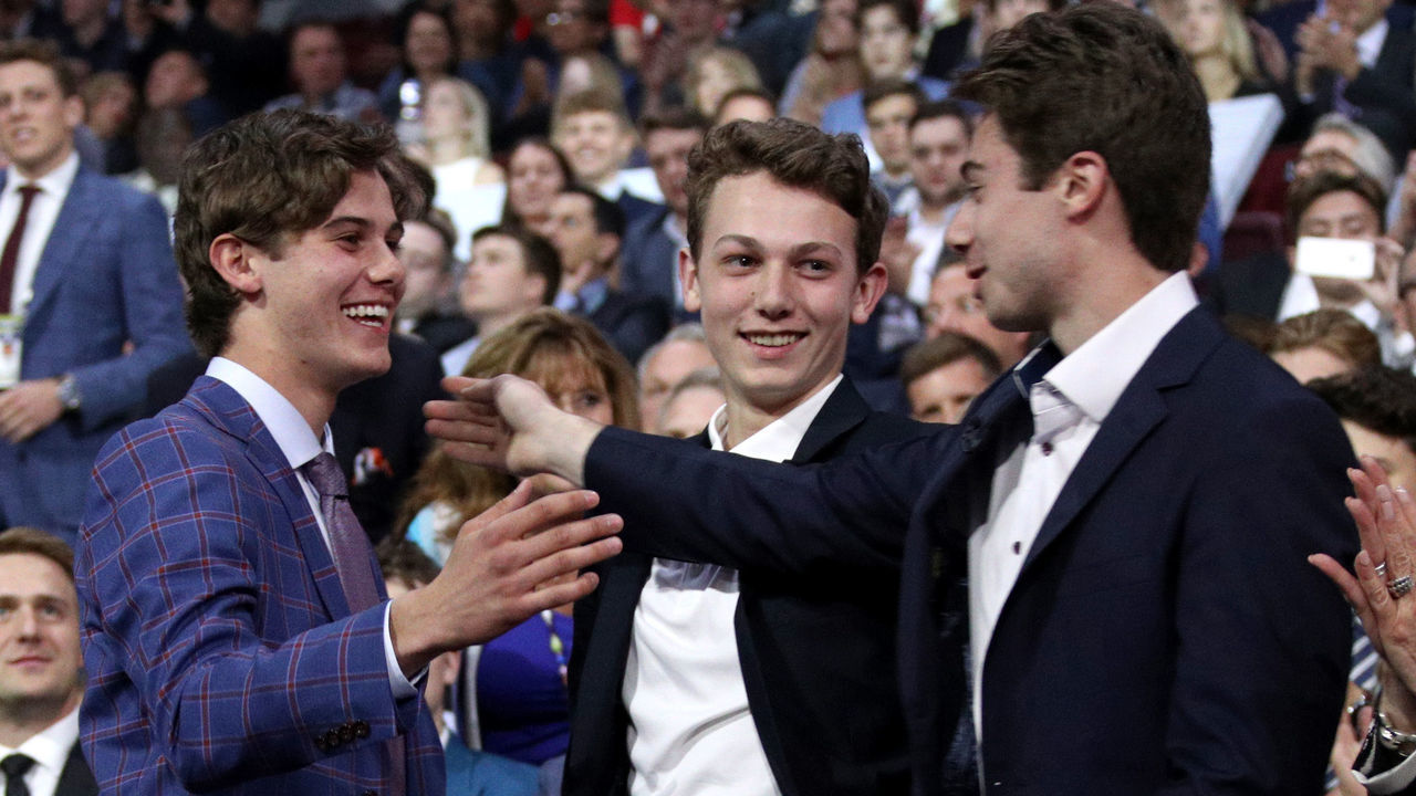 VANCOUVER, BRITISH COLUMBIA - JUNE 21: (L-R) Jack Hughes, first overall pick by the New Jersey Devils, is congratulated by his brothers Luke and Quinn Hughes during the first round of the 2019 NHL Draft at Rogers Arena on June 21, 2019 in Vancouver, Canada.