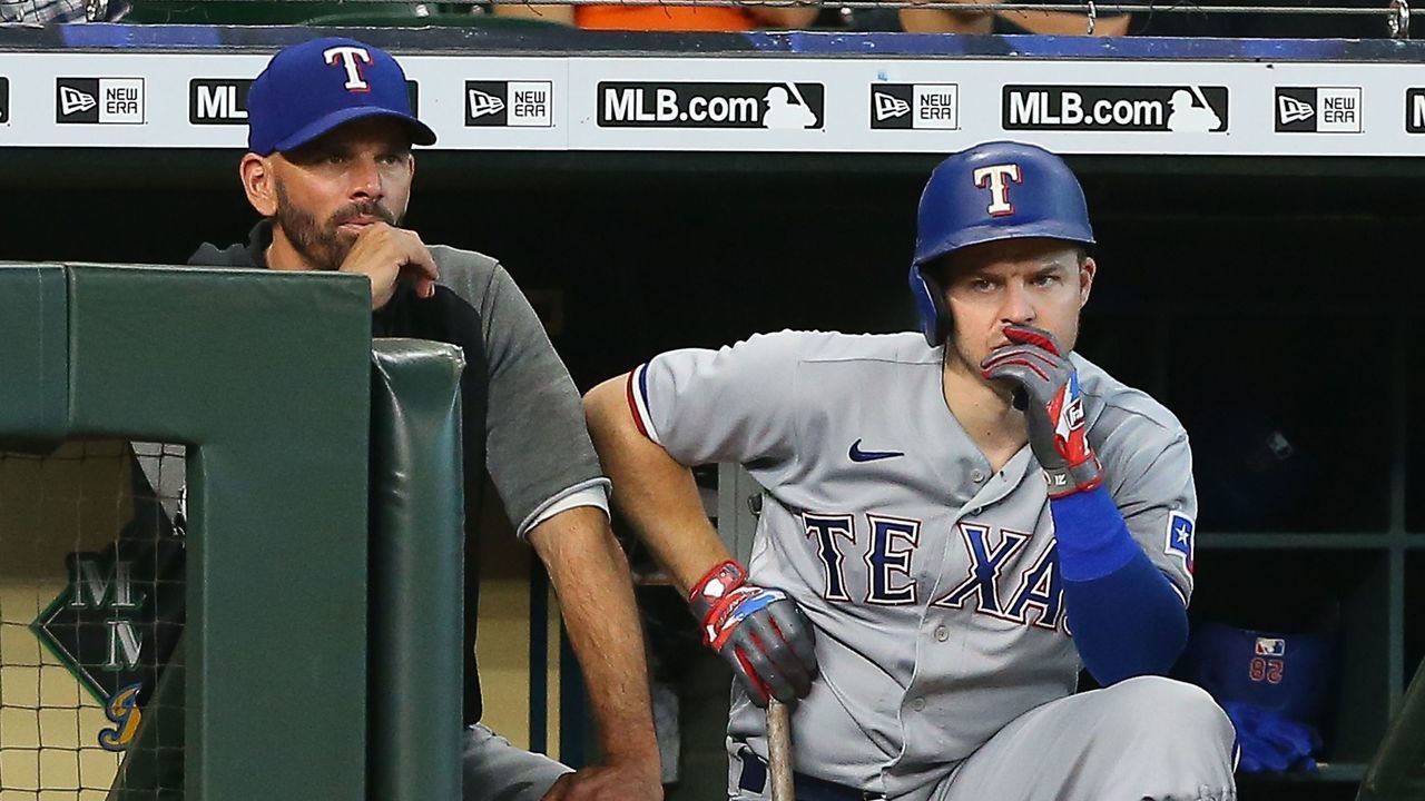 HOUSTON, TEXAS - JULY 25: Manager Chris Woodward #8 of the Texas Rangers and Brock Holt look on from the dugout against the Houston Astros at Minute Maid Park on July 25, 2021 in Houston, Texas.