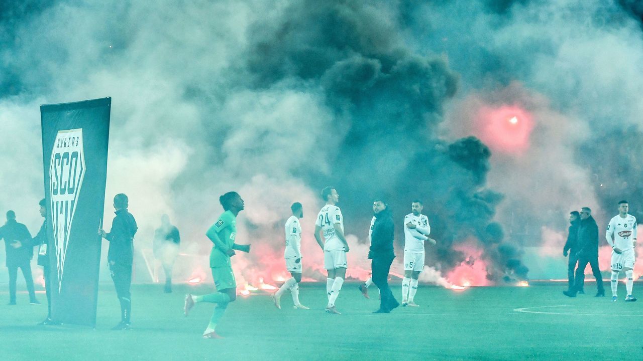 TOPSHOT - AS Saint-Etienne and SCO Angers football players react on the pitch after AS Saint-Etienne supporters launched smoke canisters to protest against the last place of their football club in the ranking of the French L1 championship, prior to the start of the French L1 football match between AS Saint-Etienne and SCO Angers at the Geoffroy Guichard stadium in Saint-Etienne, central France, on October 22, 2021. - Incidents broke out during the pre-match protocol Saint-Etienne/Angers of the 11th day of Ligue 1, caused by the ultras groups of the club stéphanois, and the kickoff of the game scheduled for 21:00 has been delayed.