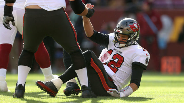 LANDOVER, MARYLAND - NOVEMBER 14: Quarterback Tom Brady #12 of the Tampa Bay Buccaneers is helped up after being hit and failing to convert on third down in the first half against the Washington Football Team at FedExField on November 14, 2021 in Landover, Maryland.