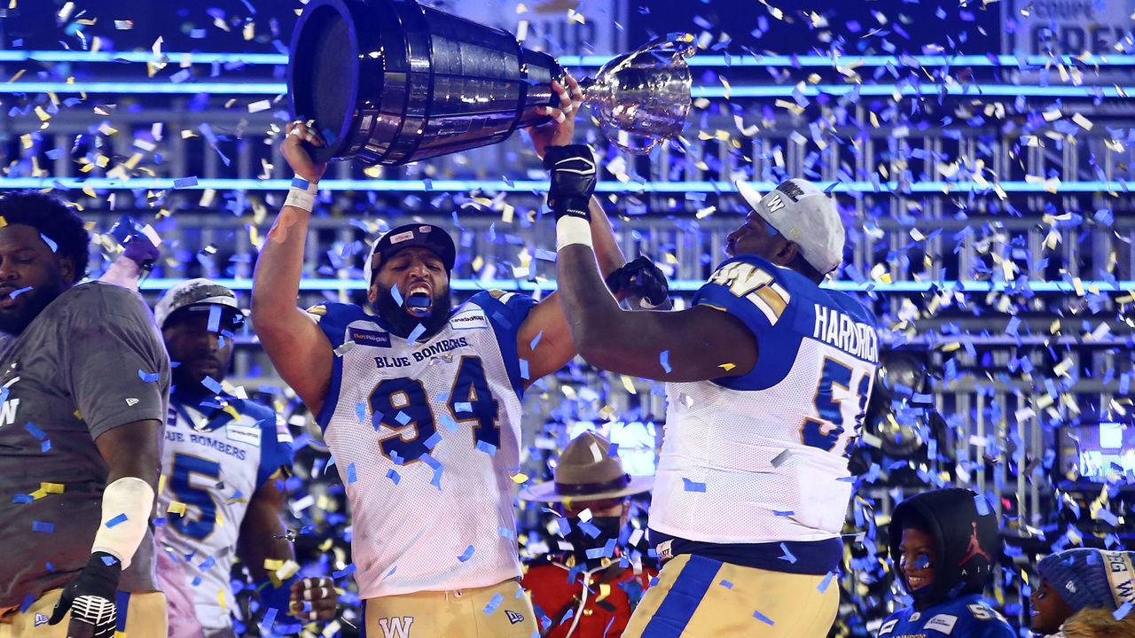HAMILTON, ON - DECEMBER 12: Jackson Jeffcoat #94 and Jermarcus Hardrick #51 of the Winnipeg Blue Bombers celebrate victory with the Grey Cup following the 108th Grey Cup CFL Championship Game against the Hamilton Tiger-Cats at Tim Hortons Field on December 12, 2021 in Hamilton, Ontario, Canada.