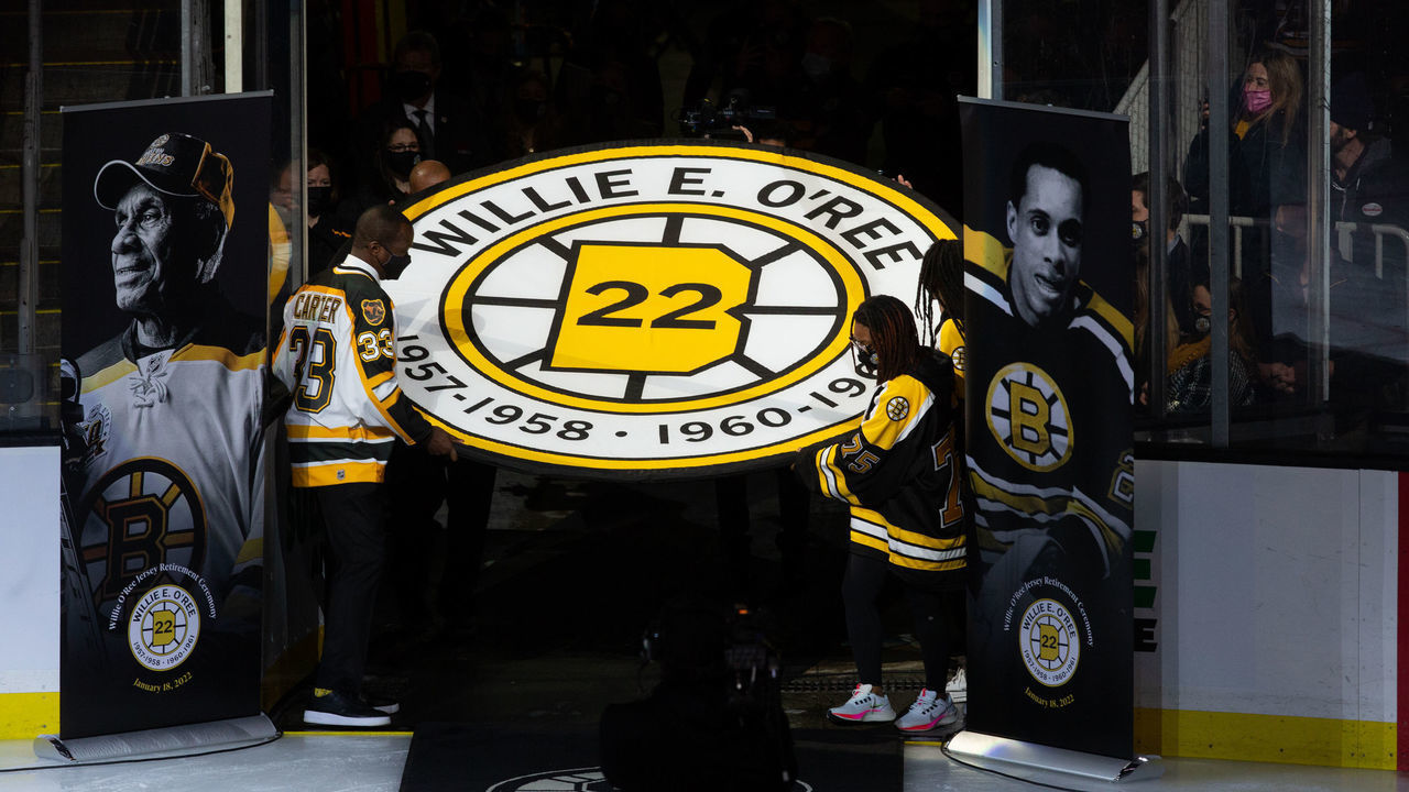 BOSTON, MA - JANUARY 18: Anson Carter helps carry the banner as former Boston Bruins player Willie O'Ree has his No. 22 jersey retired prior to the game between the Carolina Hurricanes and the Boston Bruins at the TD Garden on January 18, 2022 in Boston, Massachusetts.