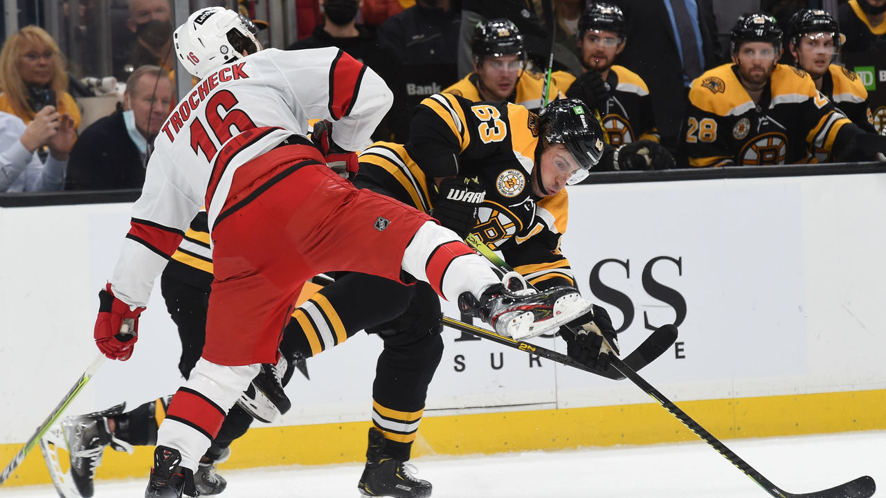 BOSTON, MA - JANUARY 18: Brad Marchand #63 of the Boston Bruins passes the puck against Vincent Trocheck #16 of the Carolina Hurricanes at the TD Garden on January 18, 2022 in Boston, Massachusetts.