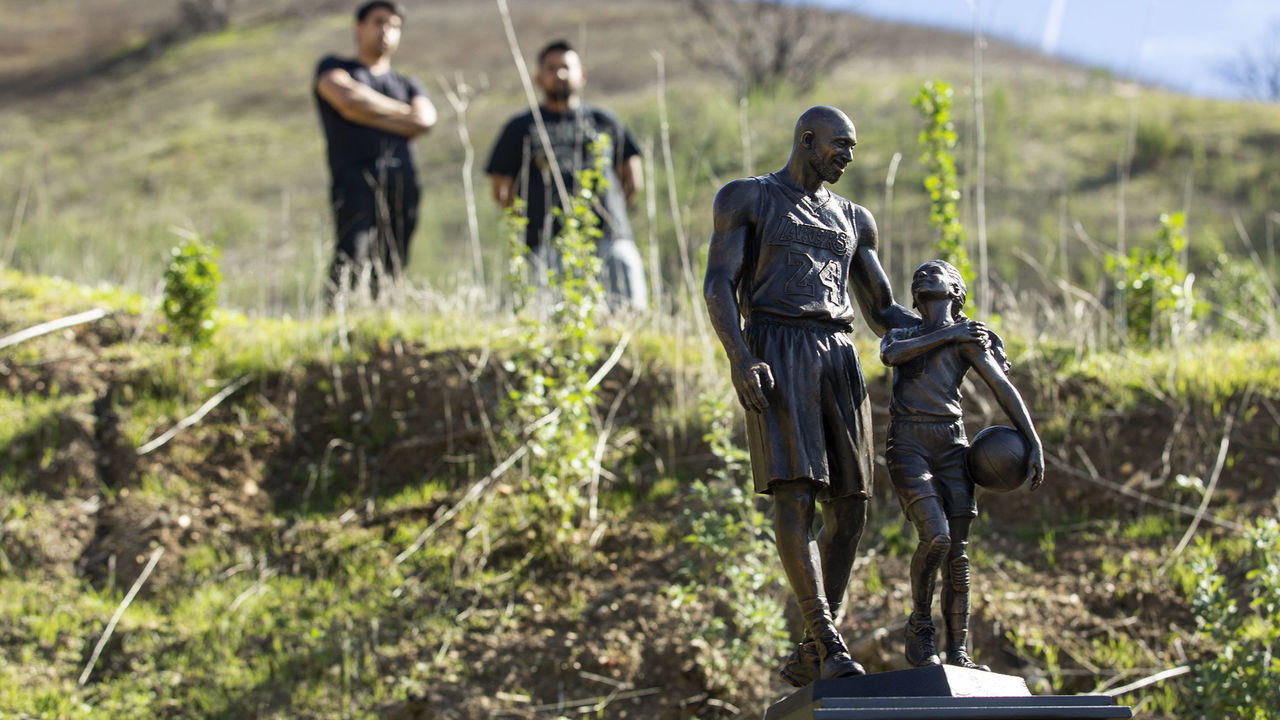 CALABASAS, CA-JANUARY 26, 2022: People visit the crash site in the hills above Las Virgenes Rd in Calabasas that took the lives of Los Angeles Lakers legend Kobe Bryant, his daughter Gianna, and 7 others exactly 2 years ago, on January 26, 2020. In foreground is a bronze statue of Bryant and his daughter Gianna. The statue, weighing about 160 pounds including the steel pedestal, was made by sculptor Dan Medina of West Hills, who had to carry the statue in sections, for the just over 1 mile hike to the crash site. He started out, using a cart and then the cart broke, forcing him to carry it to the crash site. (Mel Melcon / Los Angeles Times via Getty Images)