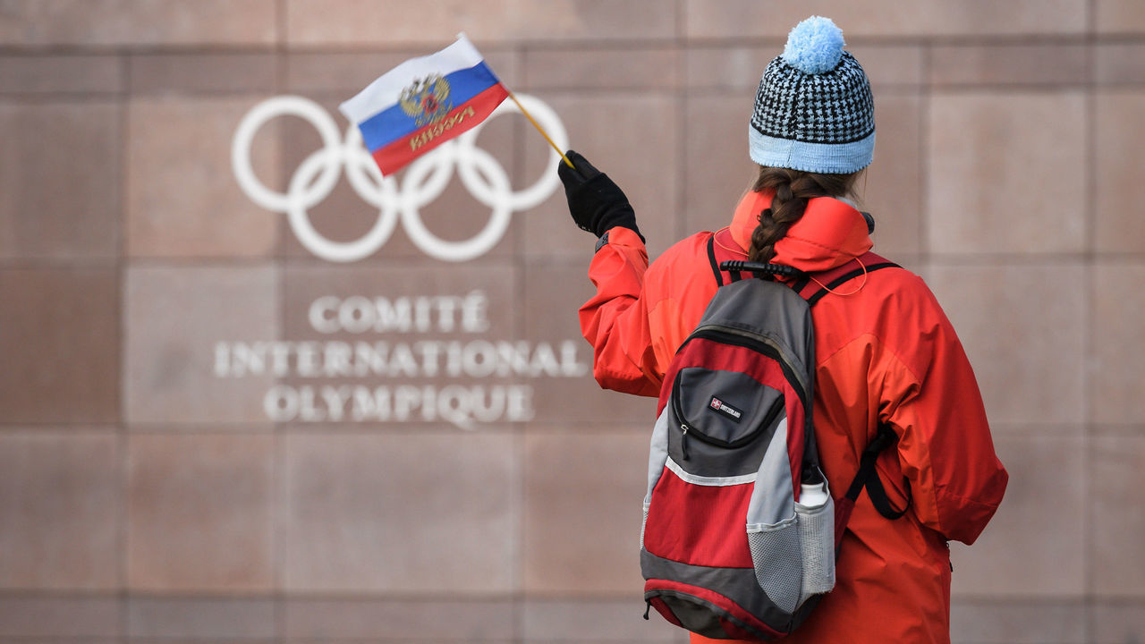 TOPSHOT - A supporter waves a Russian flag in front of the logo of the International Olympic Committee (IOC) at their headquarters on December 5, 2017 in Pully near Lausanne. - The International Olympic Committee opened a high-stakes summit on December 5 on whether to bar Russia from the Winter Olympics over allegations its medal haul at the 2014 Sochi Games was fuelled by state-sponsored doping.