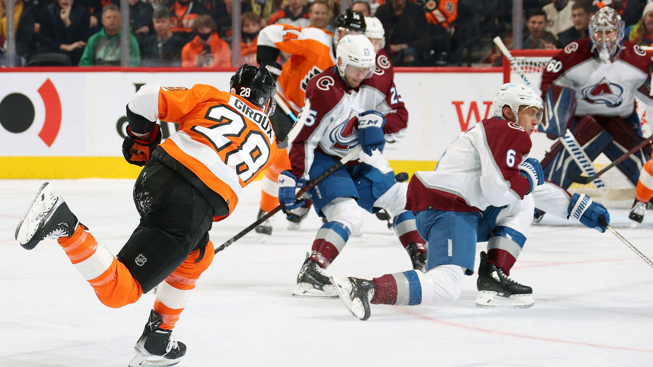 PHILADELPHIA, PA - DECEMBER 06: Claude Giroux #28 of the Philadelphia Flyers shoots the puck between Logan O Connor #25 and Erik Johnson #6 of the Colorado Avalanche at the Wells Fargo Center on December 6, 2021 in Philadelphia, Pennsylvania.