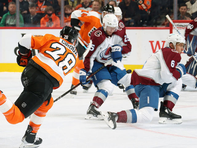 PHILADELPHIA, PA - DECEMBER 06: Claude Giroux #28 of the Philadelphia Flyers shoots the puck between Logan O Connor #25 and Erik Johnson #6 of the Colorado Avalanche at the Wells Fargo Center on December 6, 2021 in Philadelphia, Pennsylvania.