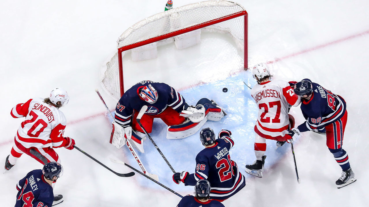 WINNIPEG, MB - APRIL 6: Michael Rasmussen #27 of the Detroit Red Wings directs the puck past goaltender Connor Hellebuyck #37 of the Winnipeg Jets for a third period goal at the Canada Life Centre on April 6, 2022 in Winnipeg, Manitoba, Canada.
