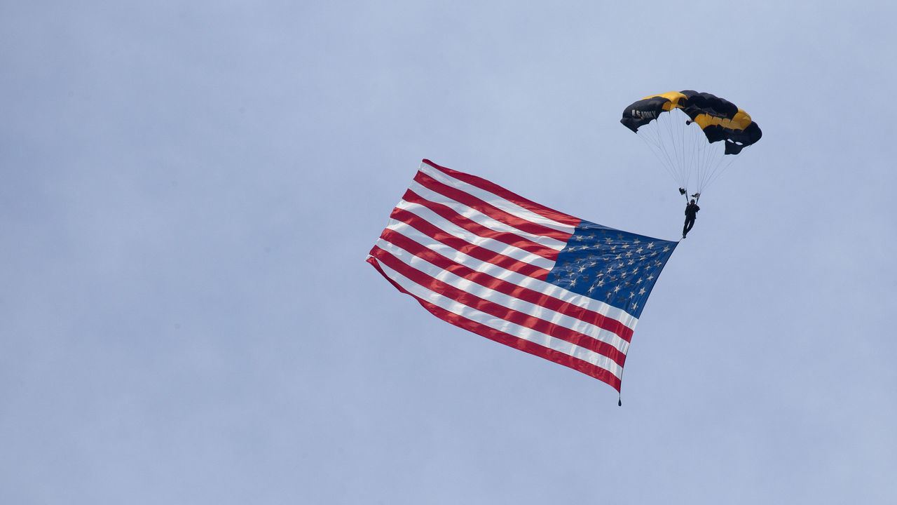 A member of the U.S. Army Golden Knights parachute team carries an American flag landing on the South Lawn of the White House during the Salute to America event in Washington, D.C., U.S., on Saturday, July 4, 2020. President Donald Trump yesterday decried what he described as efforts to eliminate U.S. history and malign heroes, lashing out at those protesting symbols they say celebrate racial injustice as he stoked culture wars over history and education. Photographer: Stefani Reynolds/CNP/Bloomberg via Getty Images