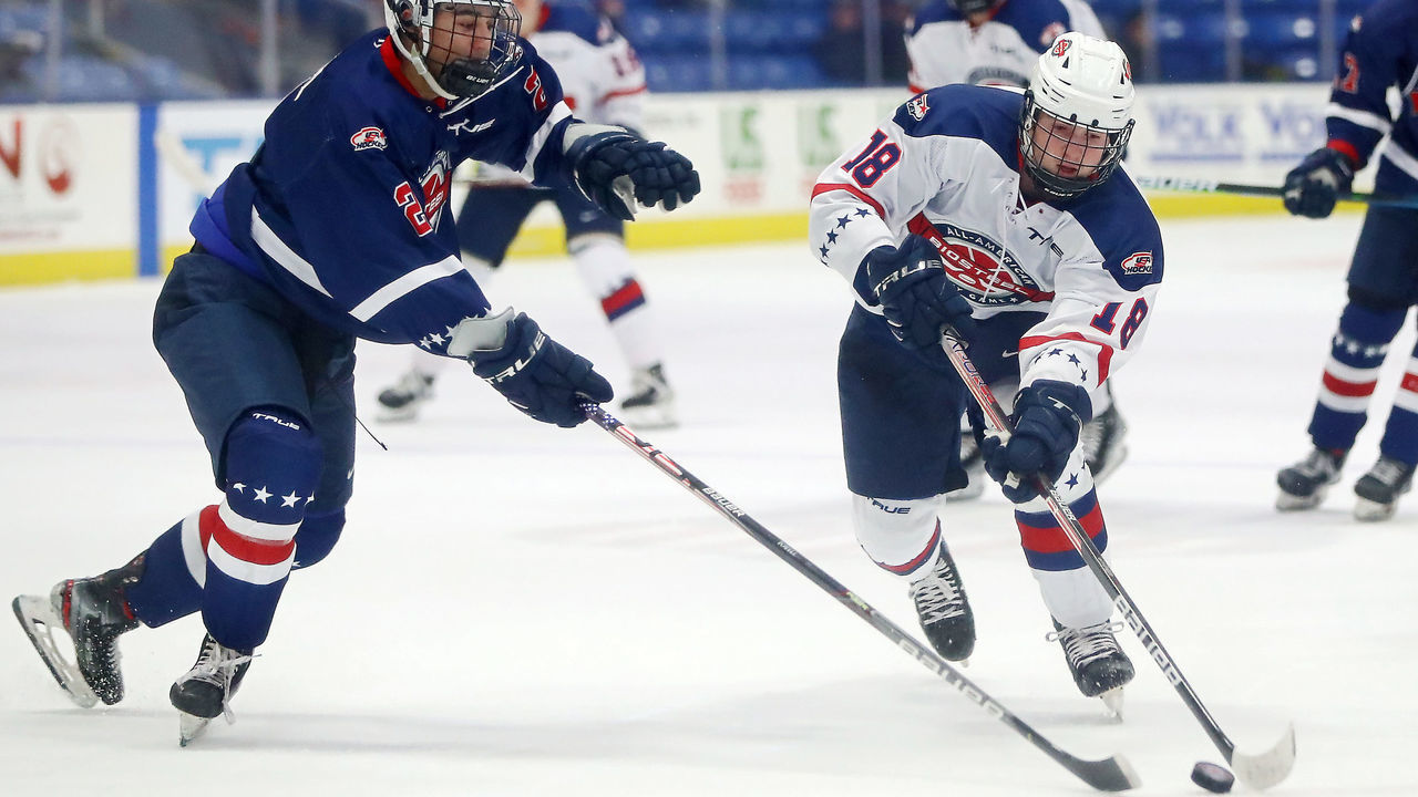 PLYMOUTH, MICHIGAN - JANUARY 17: Logan Cooley #18 of Team White passes the puck against Seamus Powell #2 of Team Blue in the second period of the USA Hockey All-American Game at USA Hockey Arena on January 17, 2022 in Plymouth, Michigan.