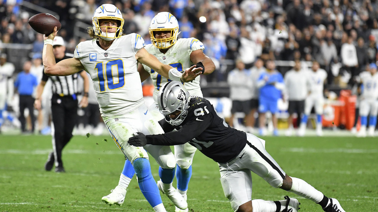 LAS VEGAS, NEVADA - JANUARY 09: Justin Herbert #10 of the Los Angeles Chargers is hit as he throws by Yannick Ngakoue #91 of the Las Vegas Raiders at Allegiant Stadium on January 09, 2022 in Las Vegas, Nevada.