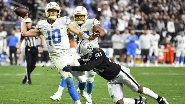 LAS VEGAS, NEVADA - JANUARY 09: Justin Herbert #10 of the Los Angeles Chargers is hit as he throws by Yannick Ngakoue #91 of the Las Vegas Raiders at Allegiant Stadium on January 09, 2022 in Las Vegas, Nevada.