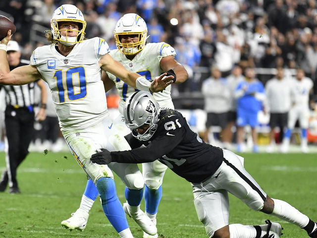 LAS VEGAS, NEVADA - JANUARY 09: Justin Herbert #10 of the Los Angeles Chargers is hit as he throws by Yannick Ngakoue #91 of the Las Vegas Raiders at Allegiant Stadium on January 09, 2022 in Las Vegas, Nevada.