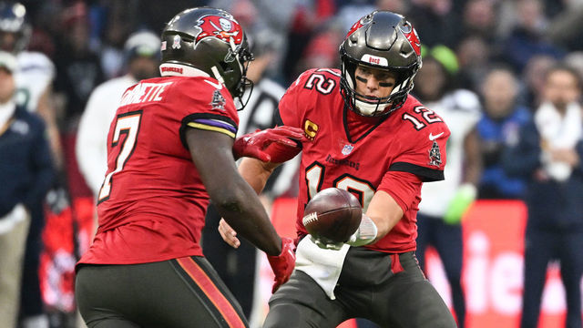 13 November 2022, Bavaria, Munich: American football: NFL professional league, Tampa Bay Buccaneers - Seattle Seahawks, main round, main round games, Matchday 10, Allianz Arena. Tom Brady (r), quarterback of the Tampa Bay Buccaneers, hands the ball to Leonard Fournette. Photo: Sven Hoppe/dpa