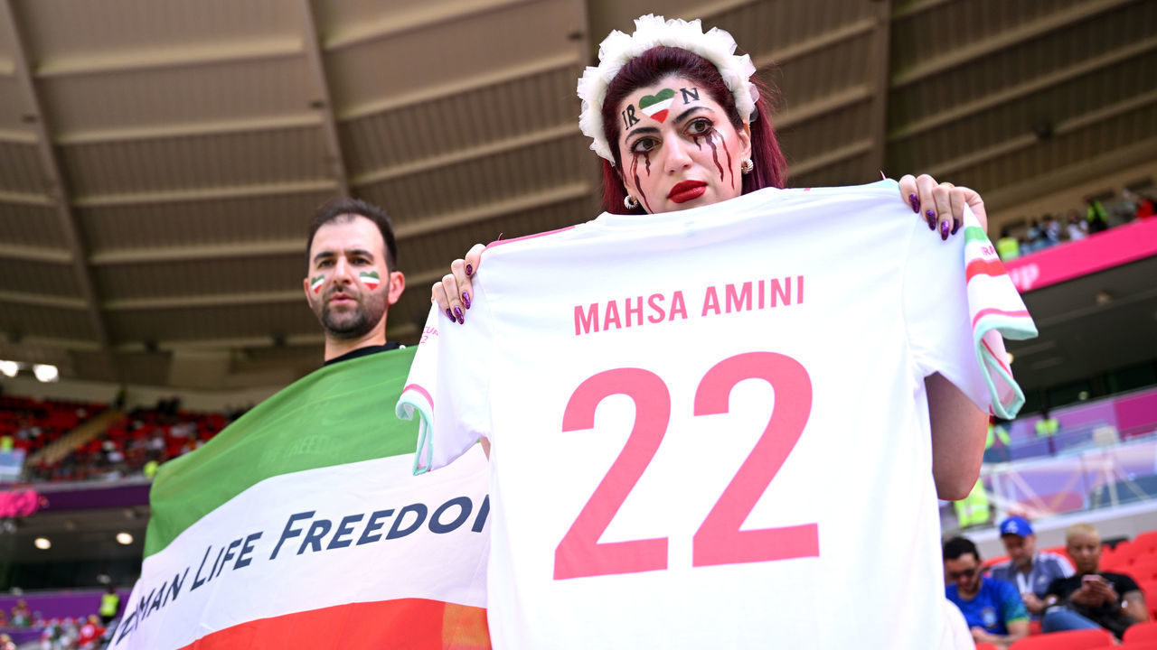 DOHA, QATAR - NOVEMBER 25: Fans hold up a shirt with the name of Mahsa Amini and a flag advocating for women's rights prior to the FIFA World Cup Qatar 2022 Group B match between Wales and IR Iran at Ahmad Bin Ali Stadium on November 25, 2022 in Doha, Qatar. People have continued demonstrating in Iran over the death of Mahsa Amini in September. Mahsa Amini fell into a coma and died after being arrested in Tehran by morality police, for allegedly violating the country's hijab rules.