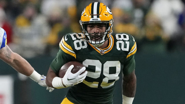 GREEN BAY, WISCONSIN - DECEMBER 19: AJ Dillon #28 of the Green Bay Packers avoids a tackle by Jalen Ramsey #5 of the Los Angeles Rams at Lambeau Field on December 19, 2022 in Green Bay, Wisconsin.