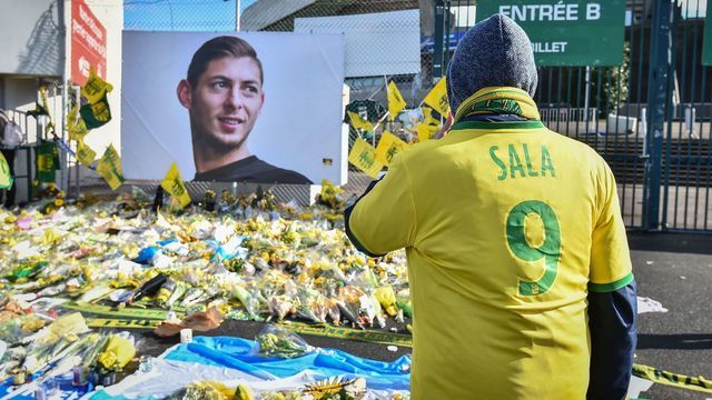 Supporters pay a tribute and look at yellow flowers displayed in front of the portrait of Argentinian forward Emiliano Sala at the Beaujoire stadium in Nantes, on February 10, 2019. - FC Nantes football club announced on February 8, 2019 that it will freeze the #9 jersey as a tribute to Cardiff City and former Nantes footballer Emiliano Sala who died in a plane crash in the English Channel on January 21, 2019.