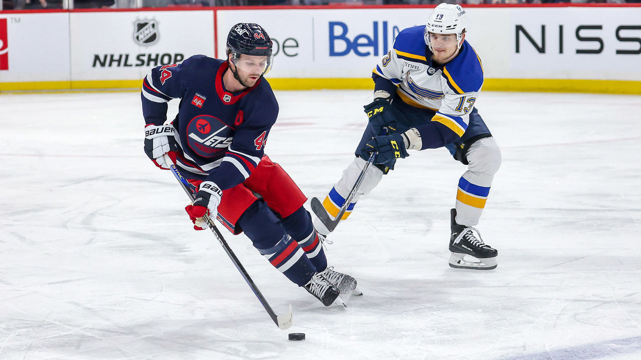 WINNIPEG, CANADA - JANUARY 30: Josh Morrissey #44 of the Winnipeg Jets plays the puck up the ice as Alexey Toropchenko #13 of the St. Louis Blues gives chase during first period action at the Canada Life Centre on January 30, 2023 in Winnipeg, Manitoba, Canada.