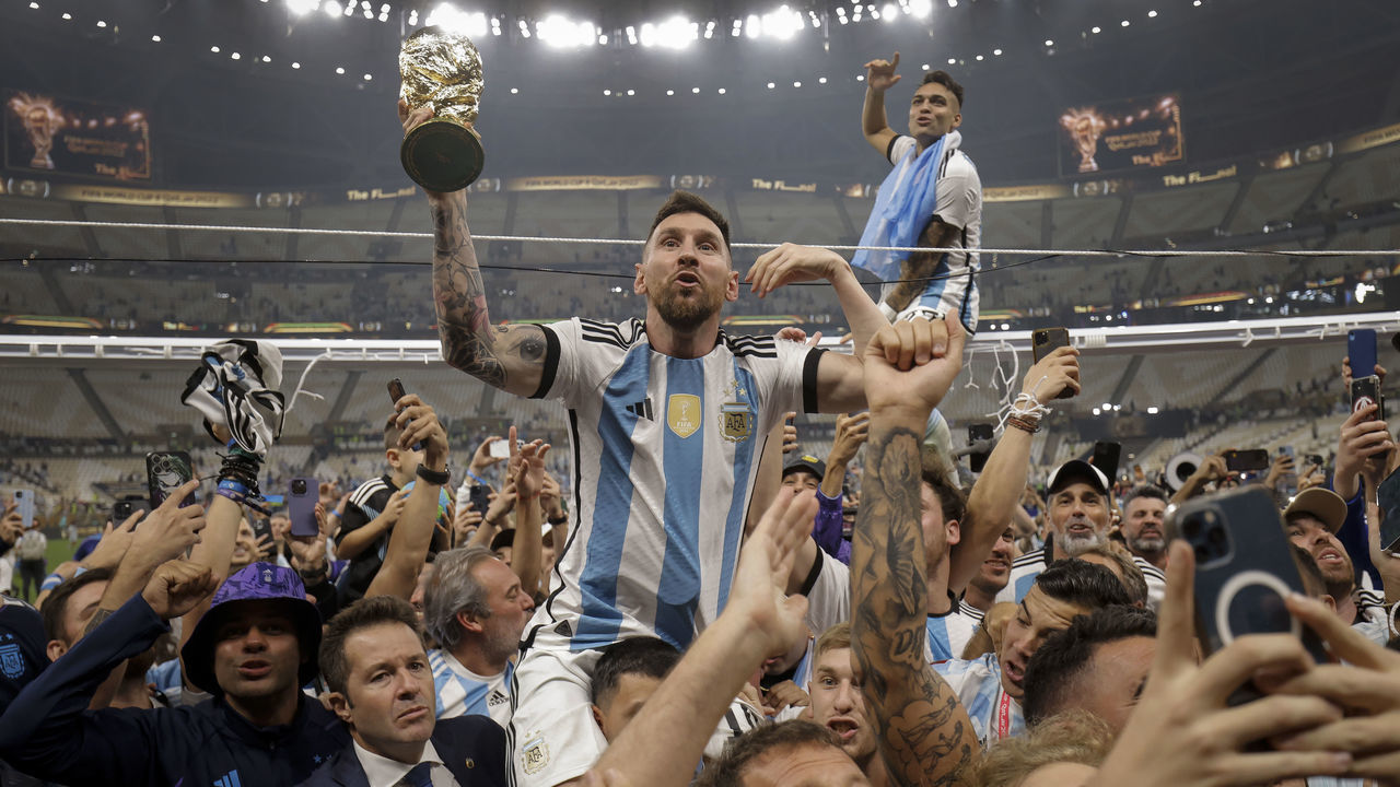 Lionel Messi of Argentina shows off the FIFA World Cup Trophy to fans while he is carried around the pitch on the shoulders of former teammate Sergio Aguero after the team's victory during the FIFA World Cup Qatar 2022 Final match between Argentina and France at Lusail Stadium on December 18, 2022 in Lusail City, Qatar.