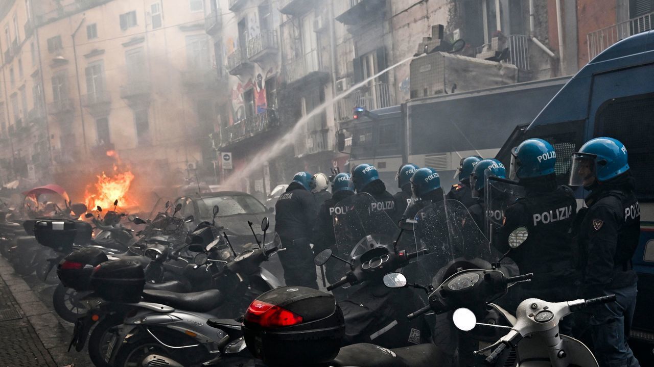 TOPSHOT - This photo obtained from Italian news agency Ansa shows a anti-riot policemen move beside a truck extinguishing the blaze of a police car after it was set on frie during clashes between Eintracht Frankfurt fans and police on March 15, 2023 in downtown Naples prior to the UEFA Champions League round of 16, second leg football match between SSC Napoli and Eintracht Frankfurt to be played at the Diego-Maradona stadium in Naples. - Eintracht Frankfurt fans clashed with police on March 15 after arriving in Naples despite not having tickets for their team's Champions League decider with Napoli.