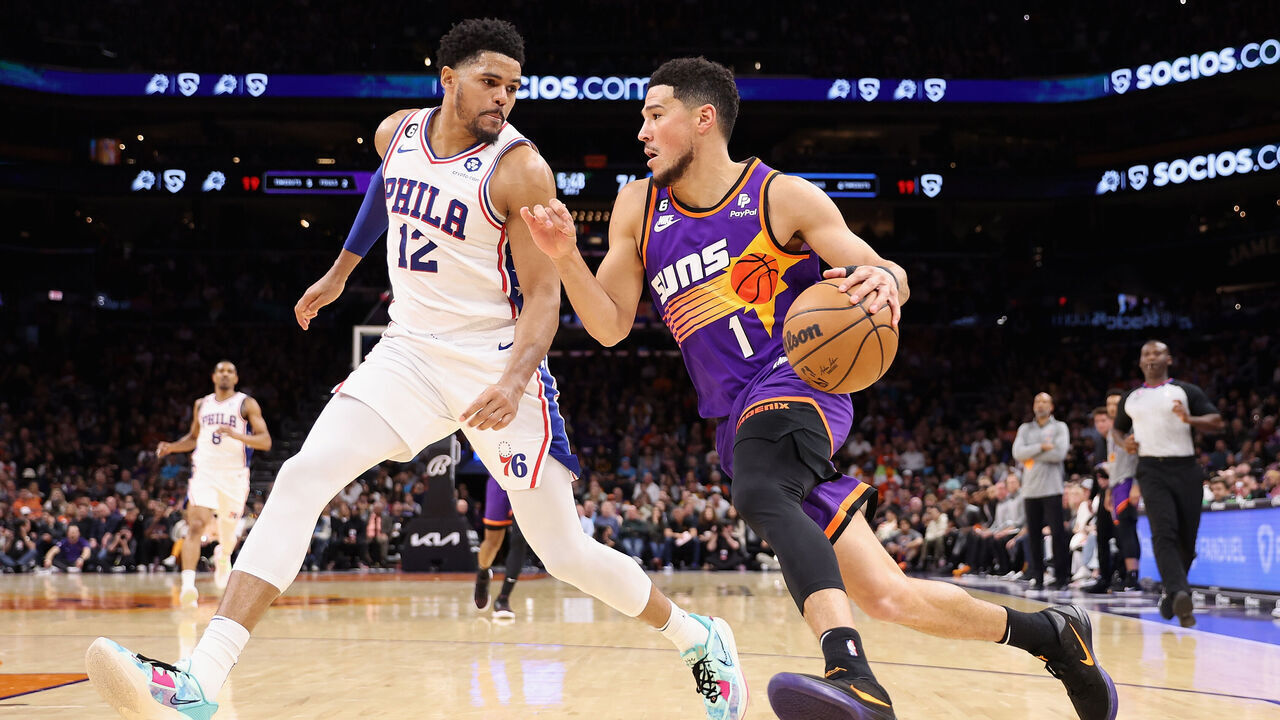 PHOENIX, ARIZONA - MARCH 25: Devin Booker #1 of the Phoenix Suns drives the ball past Tobias Harris #12 of the Philadelphia 76ers during the second half of the NBA game at Footprint Center on March 25, 2023 in Phoenix, Arizona.