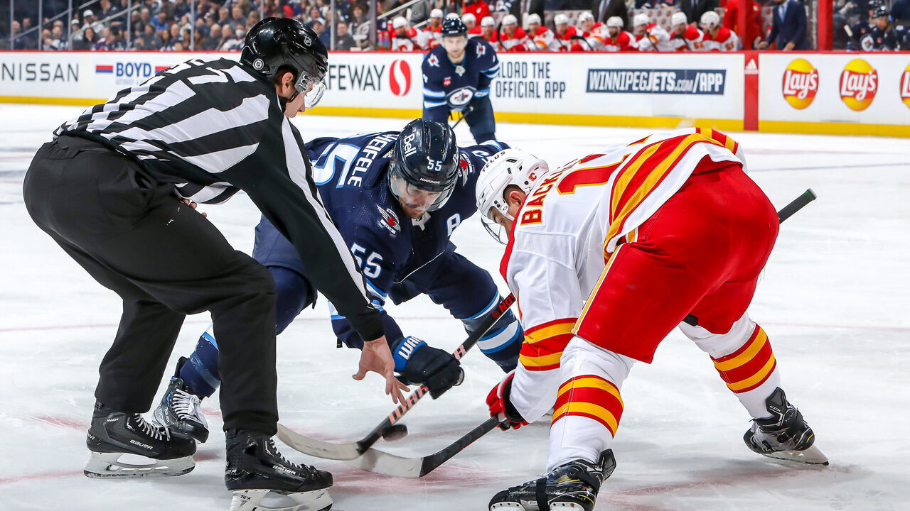 WINNIPEG, CANADA - JANUARY 3: Mark Scheifele #55 of the Winnipeg Jets takes a second period face-off against Mikael Backlund #11 of the Calgary Flames at the Canada Life Centre on January 3, 2023 in Winnipeg, Manitoba, Canada.