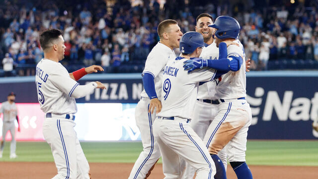 TORONTO, ON - APRIL 12: Teammates swarm George Springer #4 of the Toronto Blue Jays as they celebrate his walk-off single in the tenth inning of their MLB game against the Detroit Tigers at Rogers Centre on April 12, 2023 in Toronto, Canada.