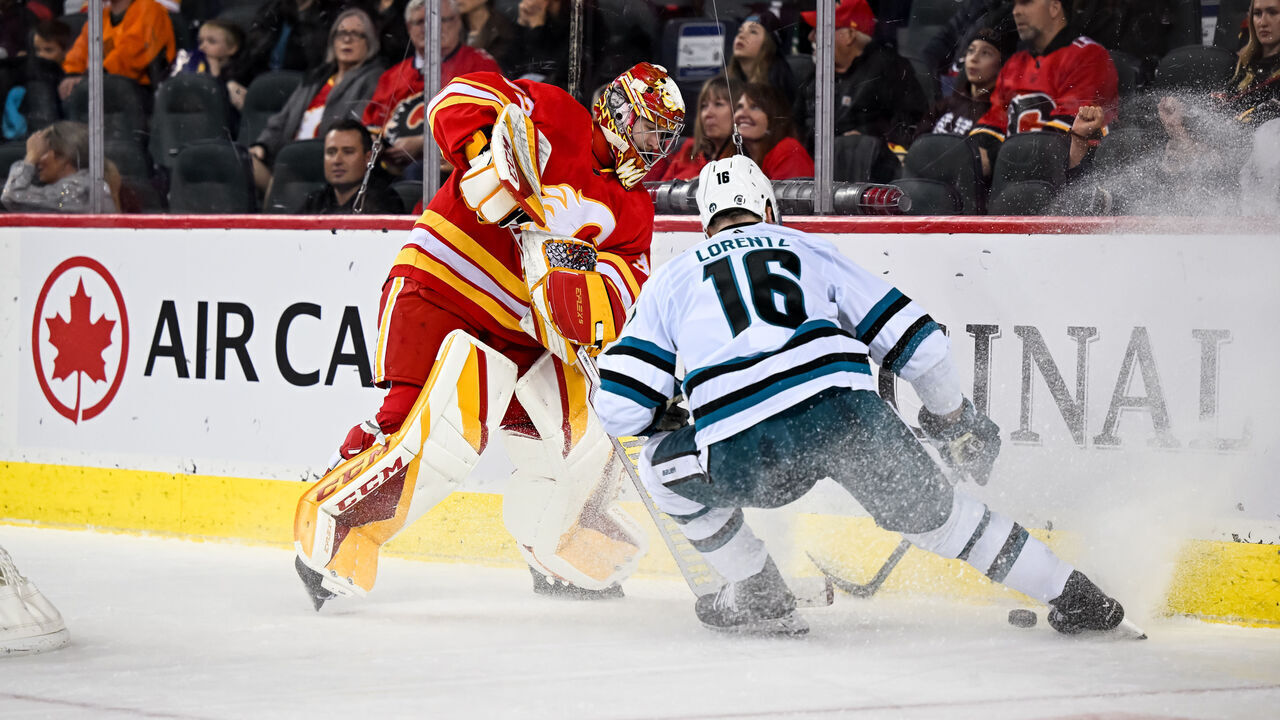 CALGARY, AB - APRIL 12: Calgary Flames Goalie Dustin Wolf (32) plays the puck behind his net as San Jose Sharks Center Steven Lorentz (16) forechecks during the second period of an NHL game between the Calgary Flames and the San Jose Sharks on April 12, 2023, at the Scotiabank Saddledome in Calgary, AB.