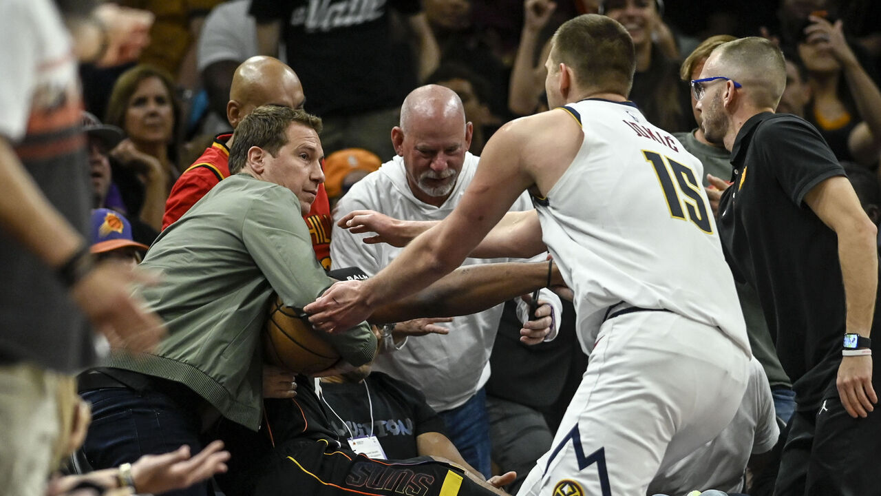 PHOENIX, AZ - MAY 7: Nikola Jokic (15) of the Denver Nuggets rushes to retrieve the game ball as Phoenix Suns owner Mat Ishbia inserts himself into the action by clutching the ball as he helps Josh Okogie (2) to his feet after Okogie flew into the stands during the second quarter at Footprint Center in Phoenix on Sunday, May 7, 2023.