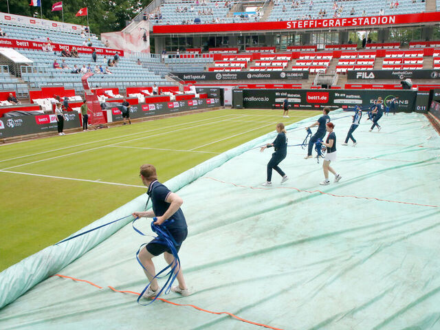 19 June 2023, Berlin: Tennis, WTA Tour 1st Round, Singles, Women, 1st Round. Tennis facility staff pull a protective sheet from the grass on center court at Steffi Graf Stadium after a break in the rain. This year's women's tennis tournament, bett1 open, will be held from June 19-25, 2023 at the Hundekehle on the LTTC Rot-Weiß facility. Photo: Wolfgang Kumm/dpa