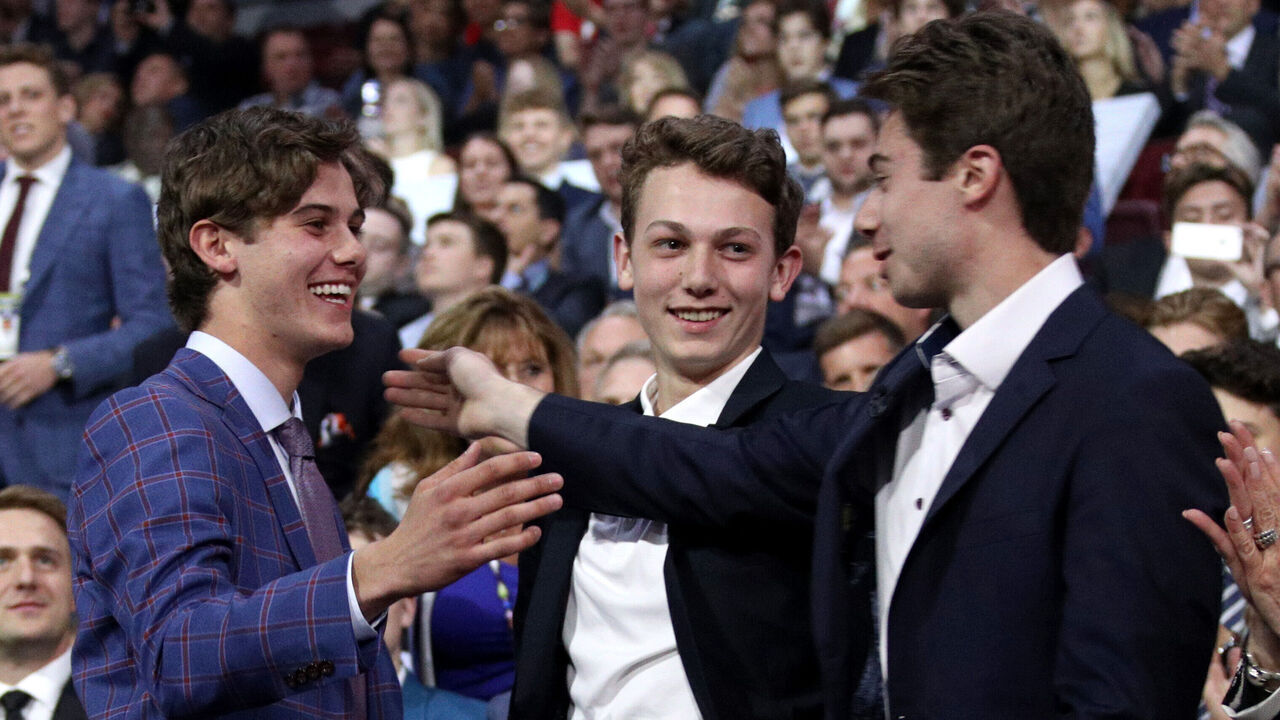VANCOUVER, BRITISH COLUMBIA - JUNE 21: (L-R) Jack Hughes, first overall pick by the New Jersey Devils, is congratulated by his brothers Luke and Quinn Hughes during the first round of the 2019 NHL Draft at Rogers Arena on June 21, 2019 in Vancouver, Canada.