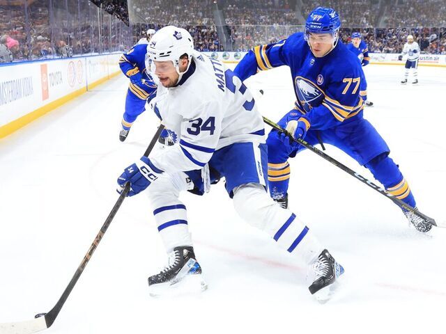 BUFFALO, NEW YORK - DECEMBER 21: Auston Matthews #34 of the Toronto Maple Leafs controls the puck against JJ Peterka #77 of the Buffalo Sabres during an NHL game on December 21, 2023 at KeyBank Center in Buffalo, New York.