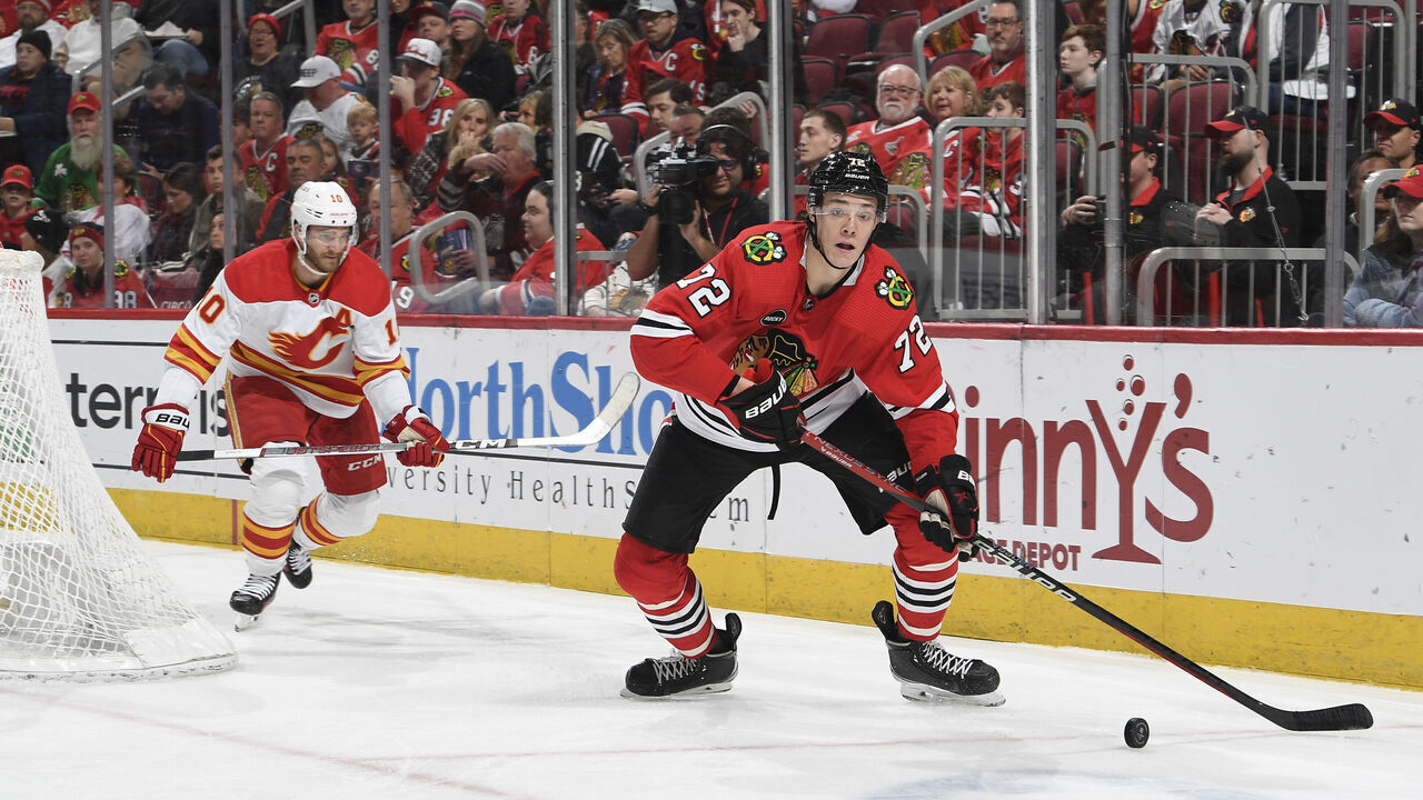 CHICAGO, ILLINOIS - JANUARY 07: Alex Vlasic #72 of the Chicago Blackhawks approaches the puck ahead of Jonathan Huberdeau #10 of the Calgary Flames in the second period at the United Center on January 07, 2024 in Chicago, Illinois.