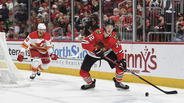 CHICAGO, ILLINOIS - JANUARY 07: Alex Vlasic #72 of the Chicago Blackhawks approaches the puck ahead of Jonathan Huberdeau #10 of the Calgary Flames in the second period at the United Center on January 07, 2024 in Chicago, Illinois.
