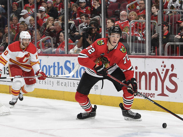 CHICAGO, ILLINOIS - JANUARY 07: Alex Vlasic #72 of the Chicago Blackhawks approaches the puck ahead of Jonathan Huberdeau #10 of the Calgary Flames in the second period at the United Center on January 07, 2024 in Chicago, Illinois.