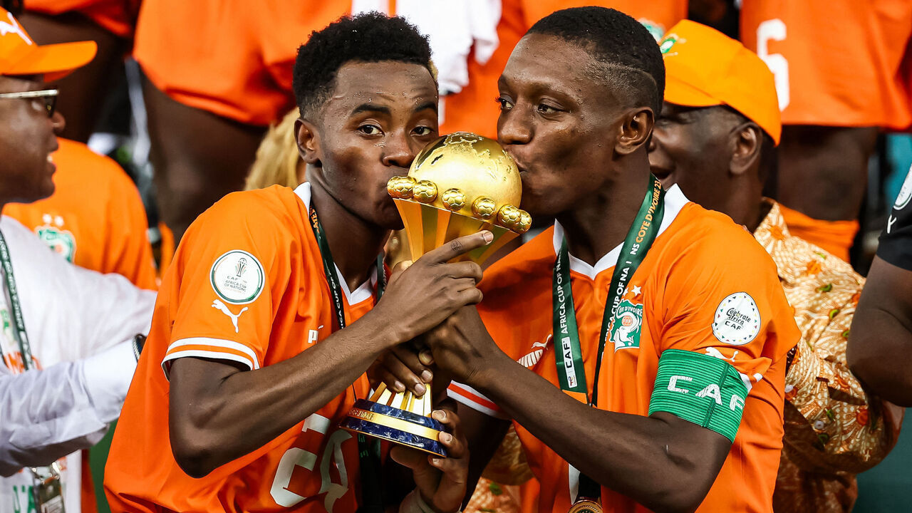 Ivory Coast's forward #15 Max-Alain Gradel (R) and Ivory Coast's forward #24 Simon Adingra (L)kiss the Africa Cup of Nations trophy on the podium after Ivory Coast won the Africa Cup of Nations (CAN) 2024 final football match between Ivory Coast and Nigeria at Alassane Ouattara Olympic Stadium in Ebimpe, Abidjan on February 11, 2024.