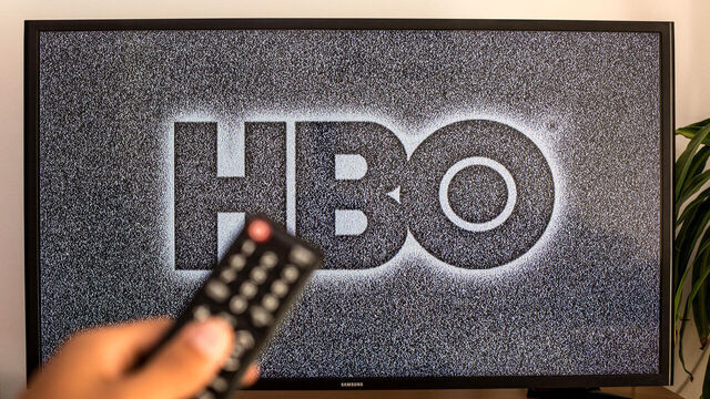 SPAIN - 2021/07/13: In this photo illustration a close-up of a hand holding a TV remote control seen displayed in front of the HBO logo on a tv in the background. (Photo Illustration by Thiago Prudencio/SOPA Images/LightRocket via Getty Images)
