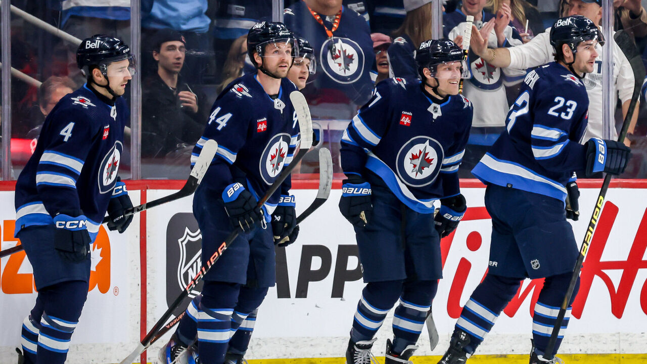 WINNIPEG, CANADA - APRIL 4: Nikolaj Ehlers #27 of the Winnipeg Jets is all smiles as he leads teammates Neal Pionk #4, Josh Morrissey #44, Cole Perfetti #91 and Sean Monahan #23 to the bench after scoring a first period goal against the Calgary Flames at the Canada Life Centre on April 4, 2024 in Winnipeg, Manitoba, Canada.