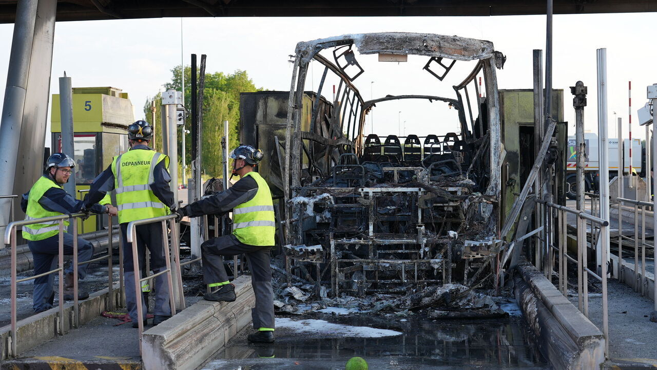 Tow-crew personnel stand by the charred remains of a bus as it sits at an A1 motorway toll in Fresnes-les-Montauban in Northern France, after a clash occurred on the roadway between supporters of Paris Saint-Germain (PSG) and Olympique Lyonnais (OL) football teams as they were travelling to Villeneuve d'Ascq near Lille for the French Cup football match final, on May 25, 2024. A bus caught fire and 20 participants were lightly injured in clashes between OL and PSG supporters at a motorway toll near Arras, hours before the French cup final opposing the two teams.
