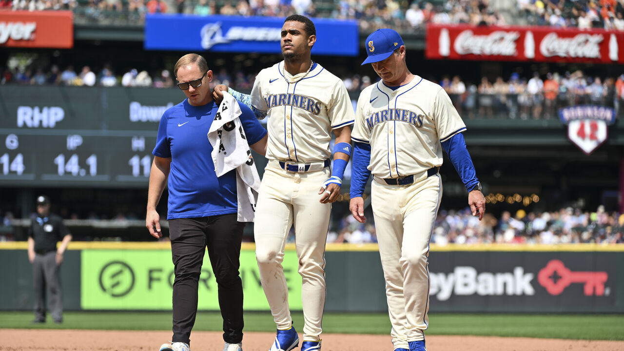 SEATTLE, WASHINGTON - JULY 21: Julio Rodriguez #44 of the Seattle Mariners is helped off the field by manager Scott Servais and the athletic training staff during the sixth inning against the Houston Astros at T-Mobile Park on July 21, 2024 in Seattle, Washington.