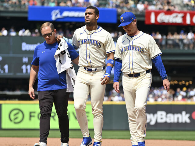 SEATTLE, WASHINGTON - JULY 21: Julio Rodriguez #44 of the Seattle Mariners is helped off the field by manager Scott Servais and the athletic training staff during the sixth inning against the Houston Astros at T-Mobile Park on July 21, 2024 in Seattle, Washington.