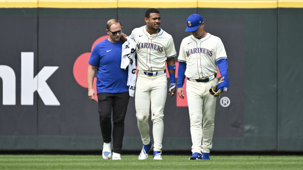 SEATTLE, WASHINGTON - JULY 21: Julio Rodriguez #44 of the Seattle Mariners is helped off the field by manager Scott Servais and the athletic training staff during the sixth inning against the Houston Astros at T-Mobile Park on July 21, 2024 in Seattle, Washington.
